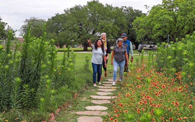 4 people walking through a green garden.