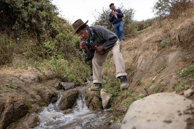 Eufronio Obispo Rojas and Luis Salinas bend over a small stream during a water celebration ceremony.